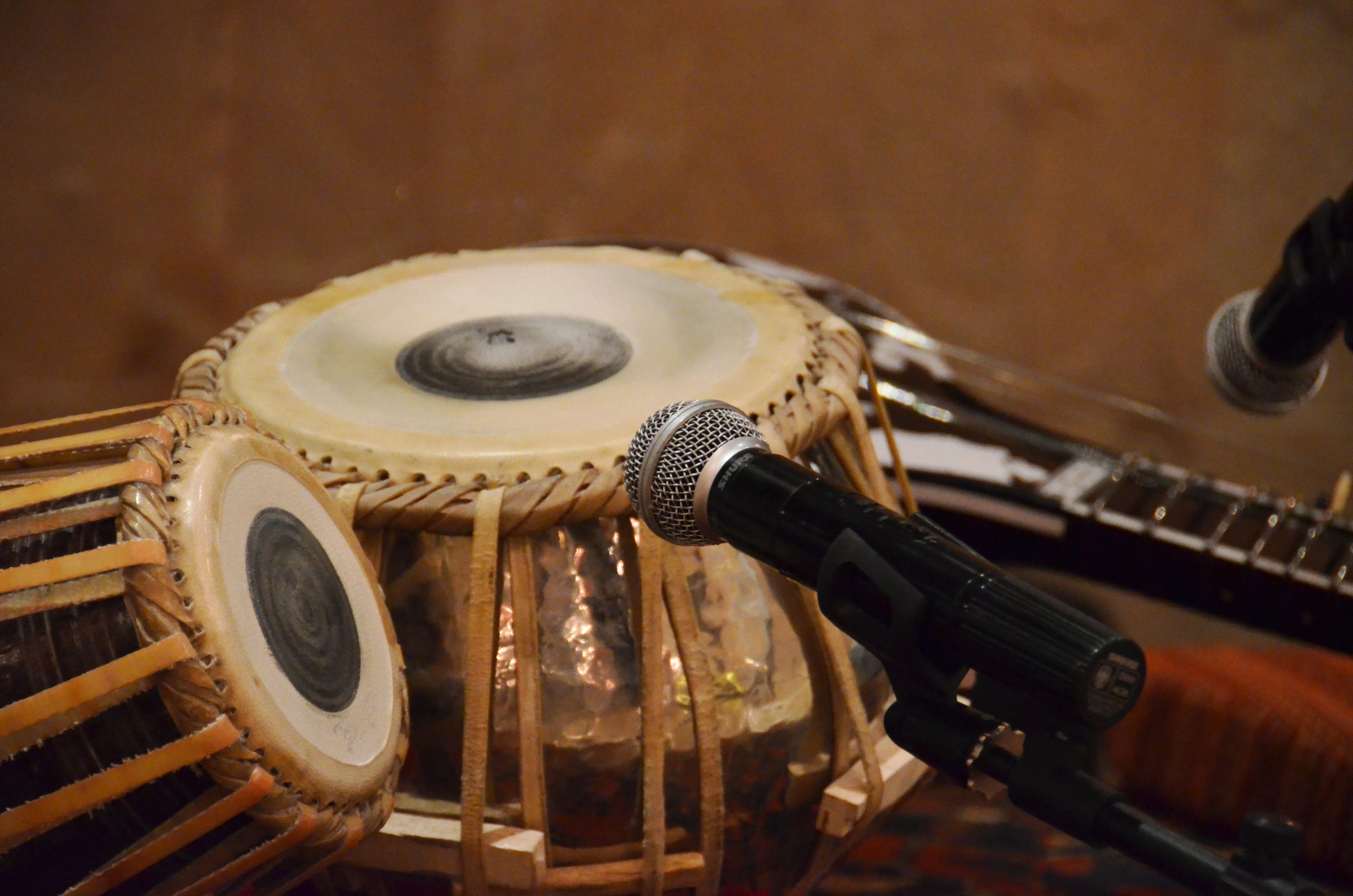 A pair of tabla, their heads marked with black syahi, a microphone angled toward them.
